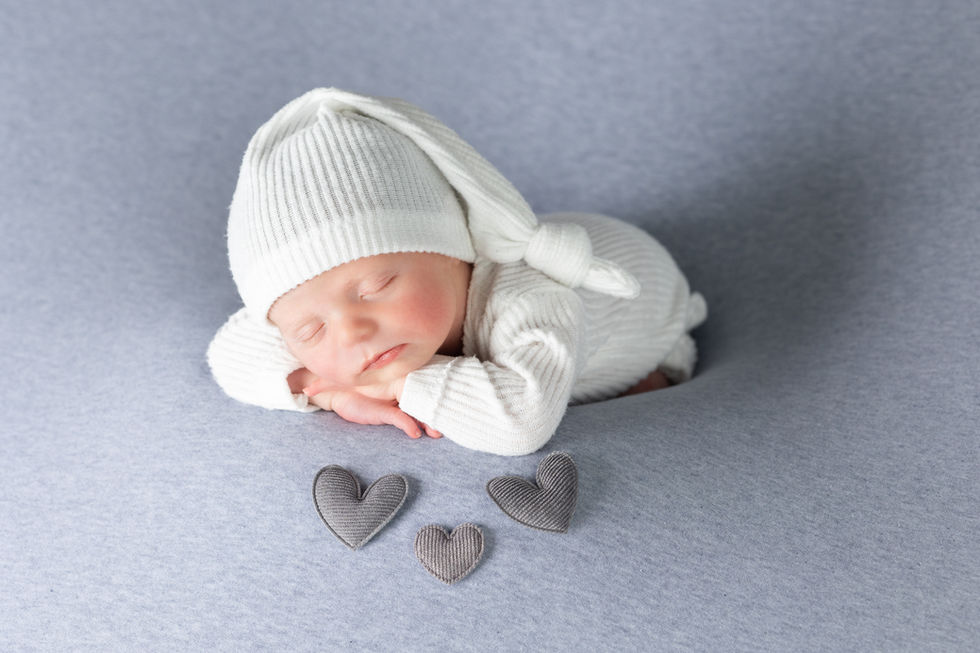 Fotografía newborn en Zaragoza de bebé recién nacido con gorro blanco sobre fondo gris con corazones