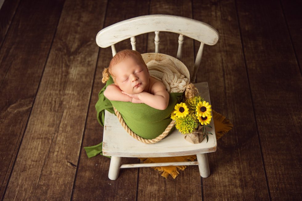 Bebé recién nacido durmiendo en una mecedora blanca con girasoles durante una sesión de fotografía newborn en Zaragoza
